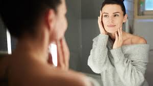 Woman looking in mirror while completing skincare routine in lockdown